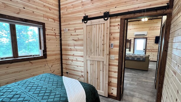 Una habitación con paneles de madera, una cama, una puerta corredera y vistas a otra habitación.