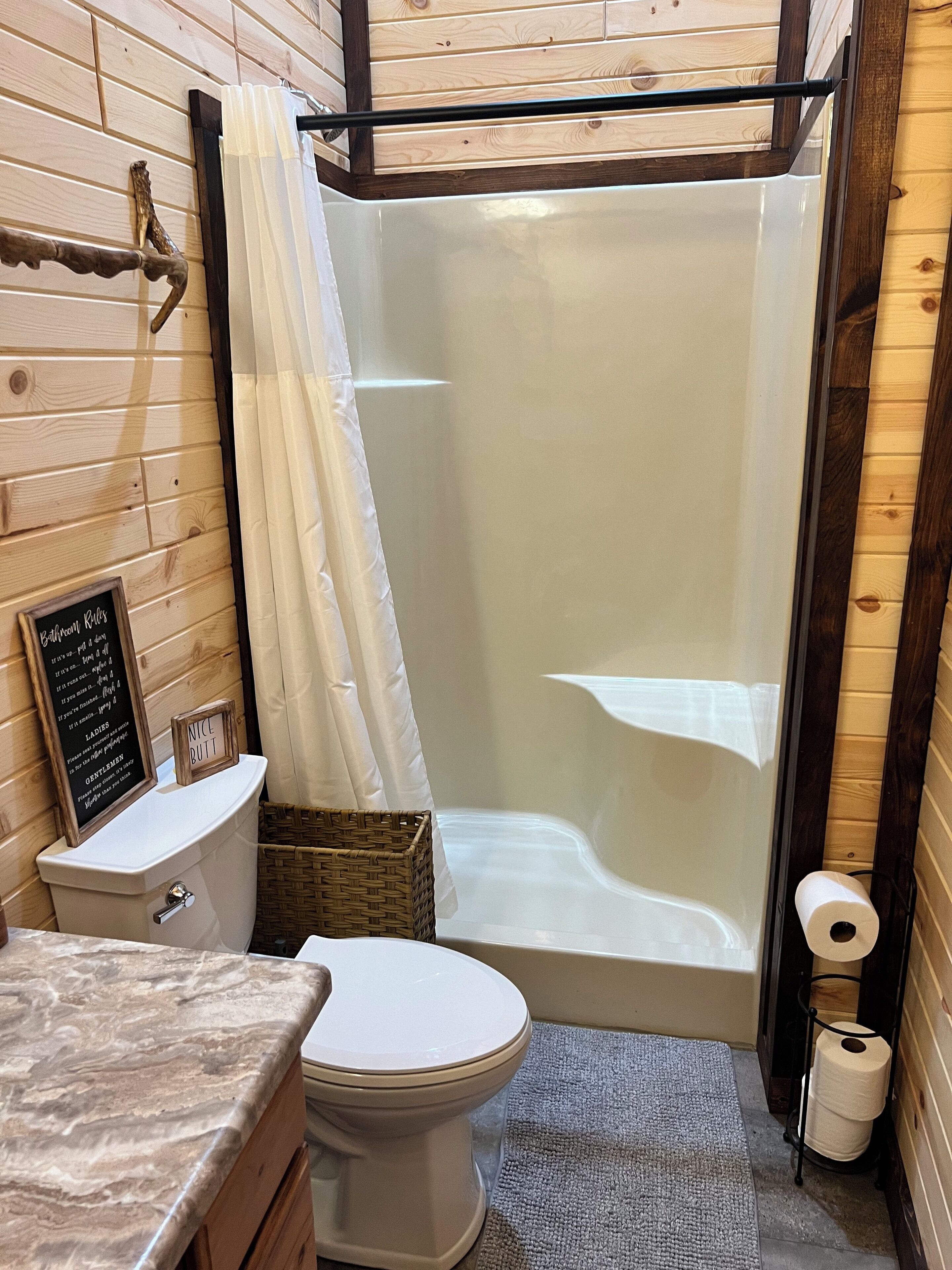 Ein Badezimmer mit Toilette, Dusche, einer Holzwand, einem Korb und einem Schild.