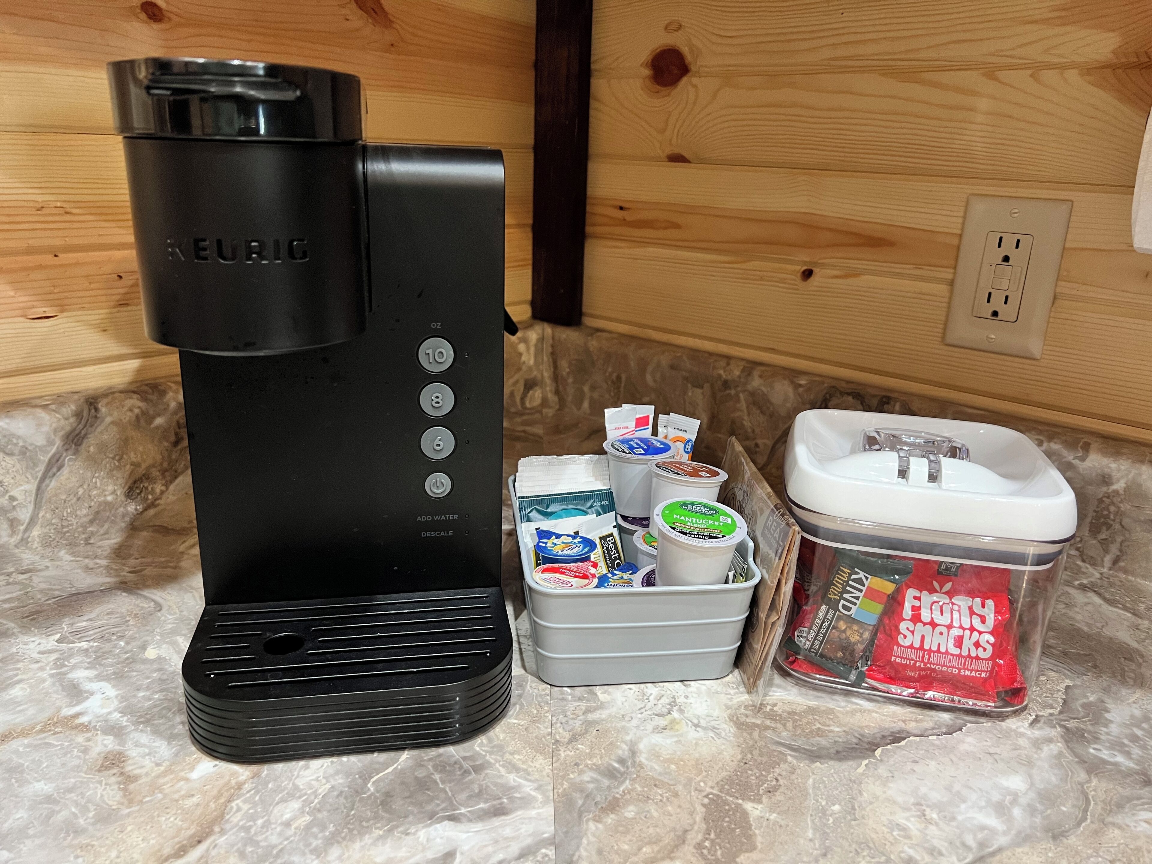 A Keurig coffee maker, a container with coffee pods, and a container with snacks.