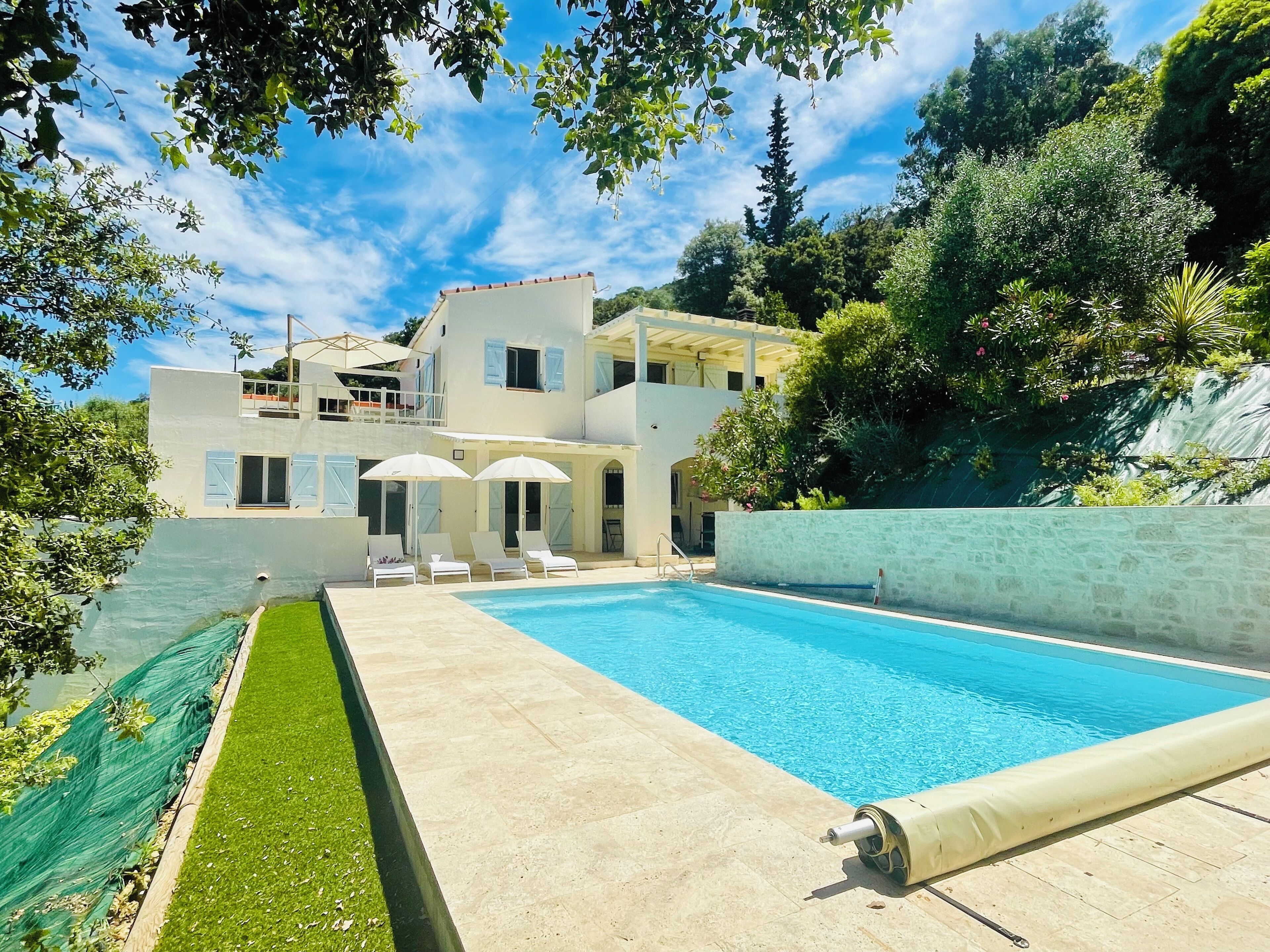 Uma área de piscina com piscina azul límpida, gramado e um edifício com várias janelas e varanda.