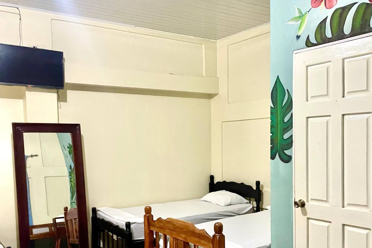 Een kamer met twee bedden, een houten hoofdbord, een betegelde vloer, een witte deur en een muur met een bloemenreliëf.