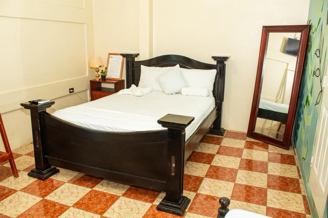 Una cama bien hecha con sábanas blancas, cabecera de madera y suelo a cuadros.