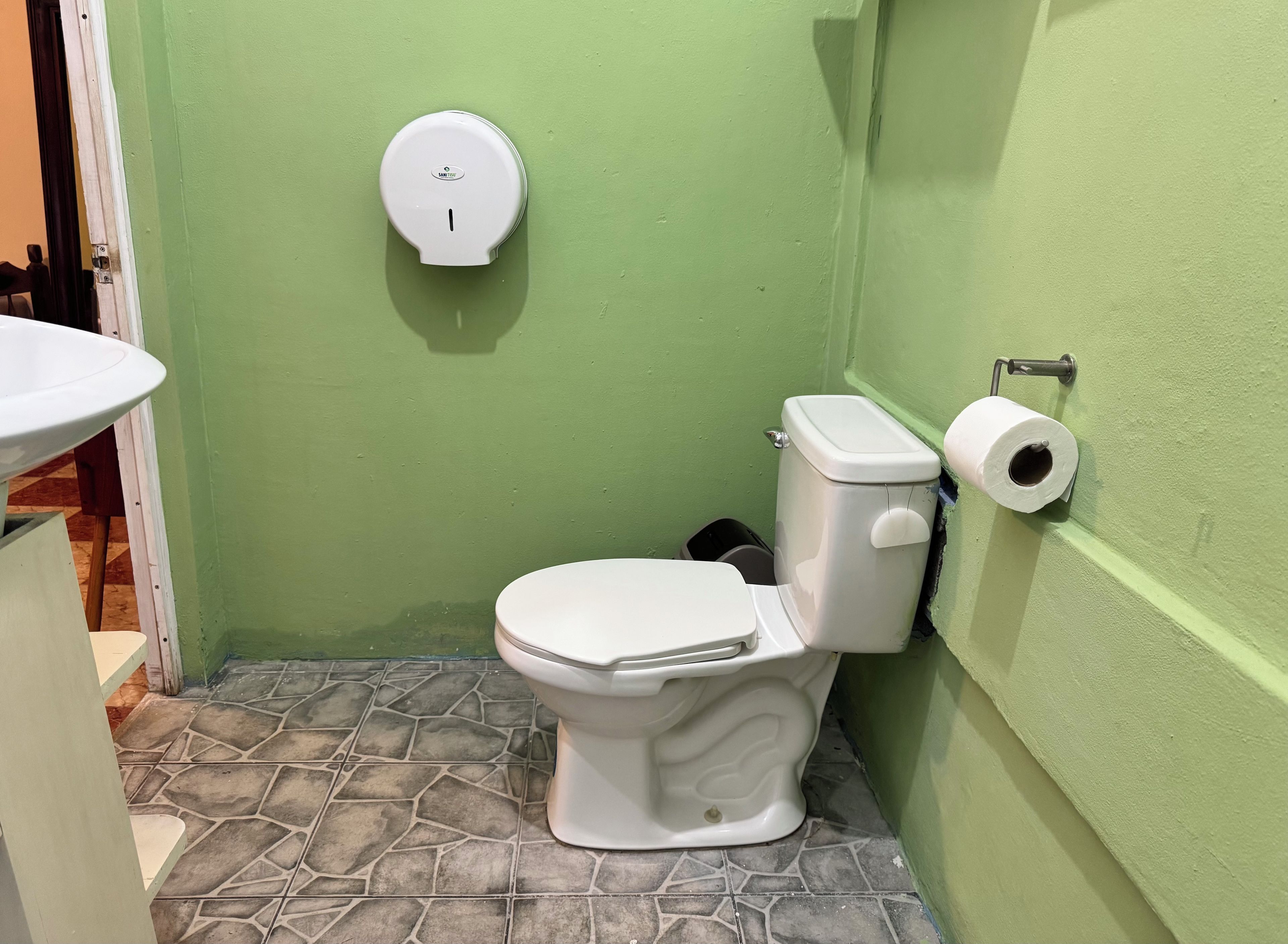 A bathroom with a toilet, a toilet paper holder, and a hand sanitizer dispenser on the wall.