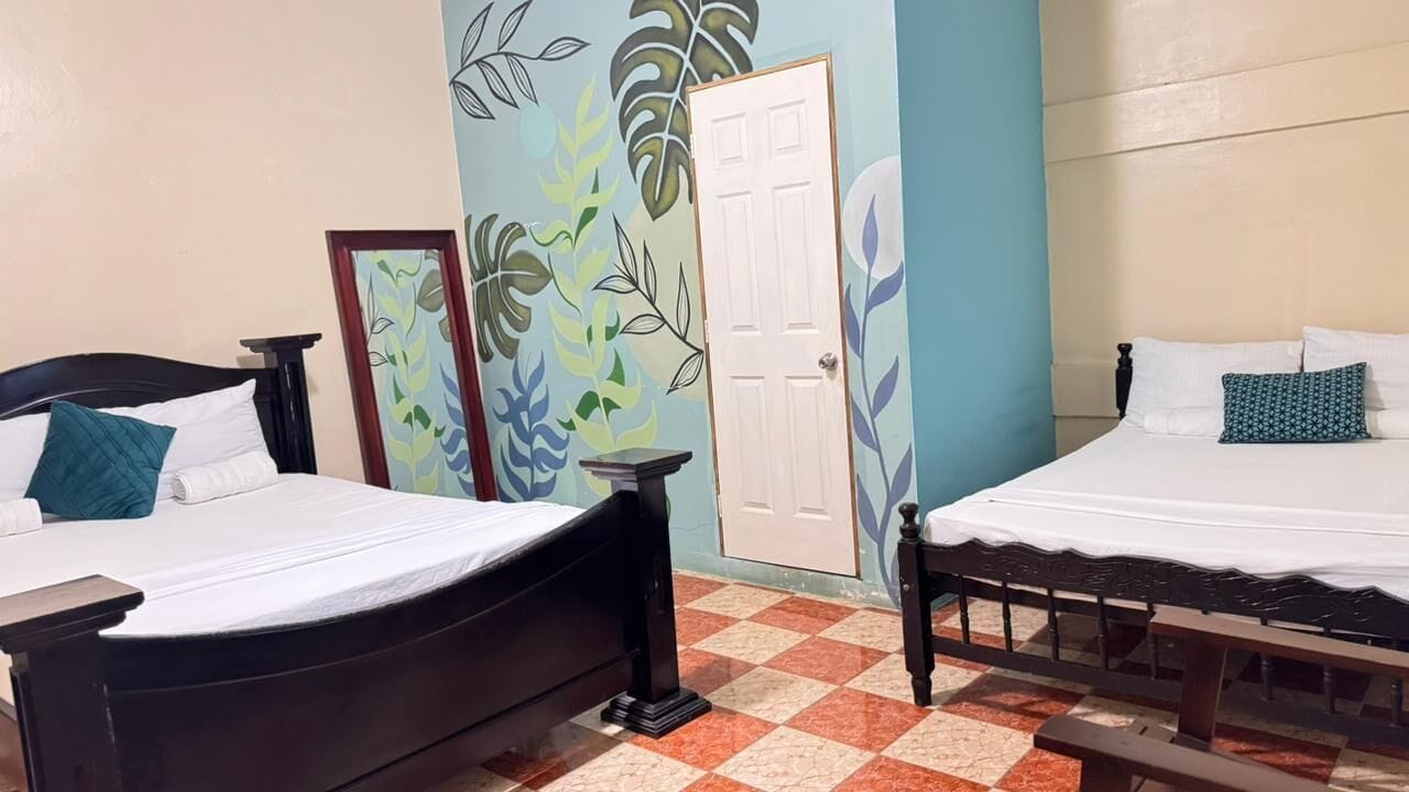 Two single beds with wooden frames, a tiled floor, a door, and a wall with a leaf pattern.