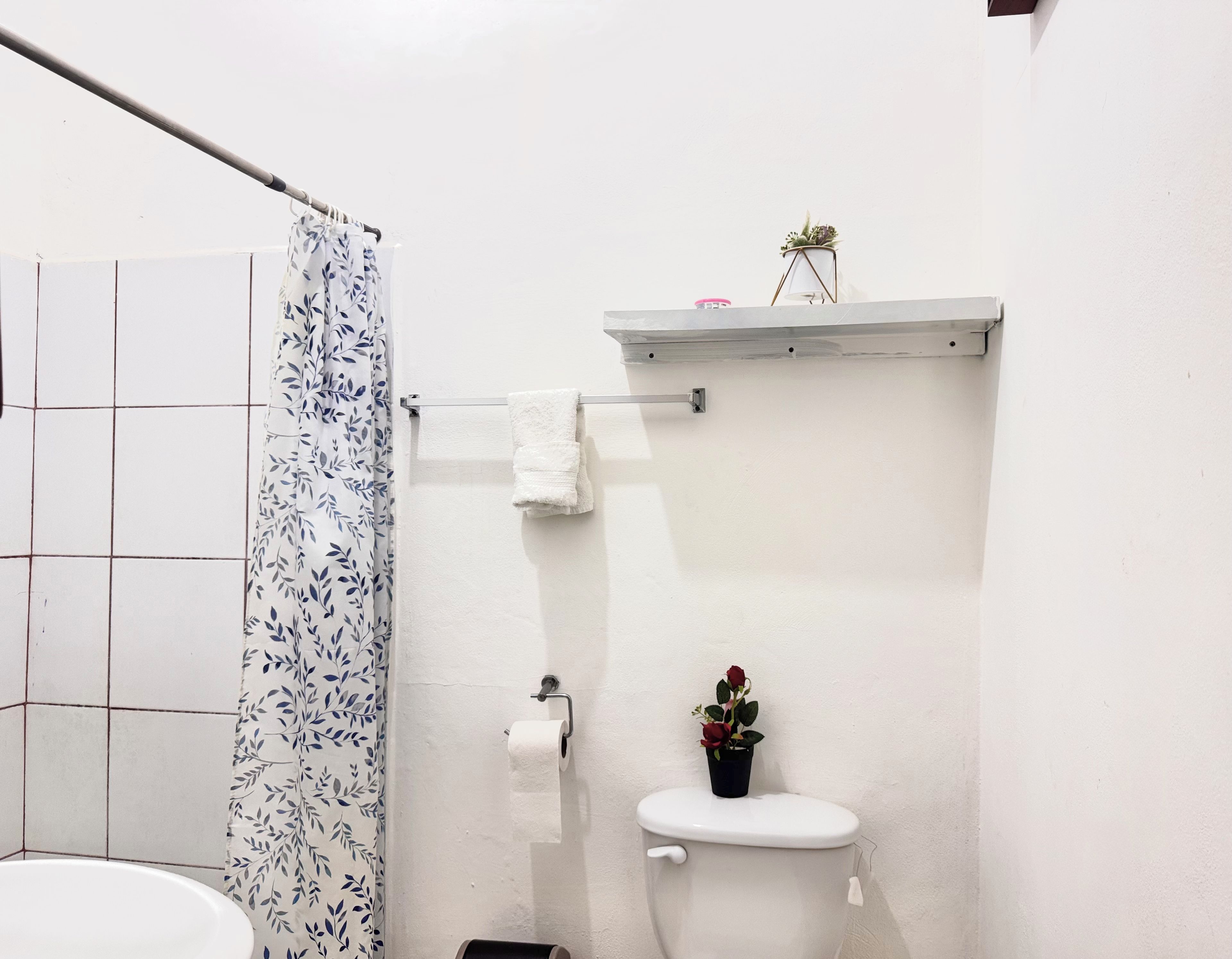 A bathroom with a toilet, a shower curtain, a towel rack, and a small shelf with a plant.