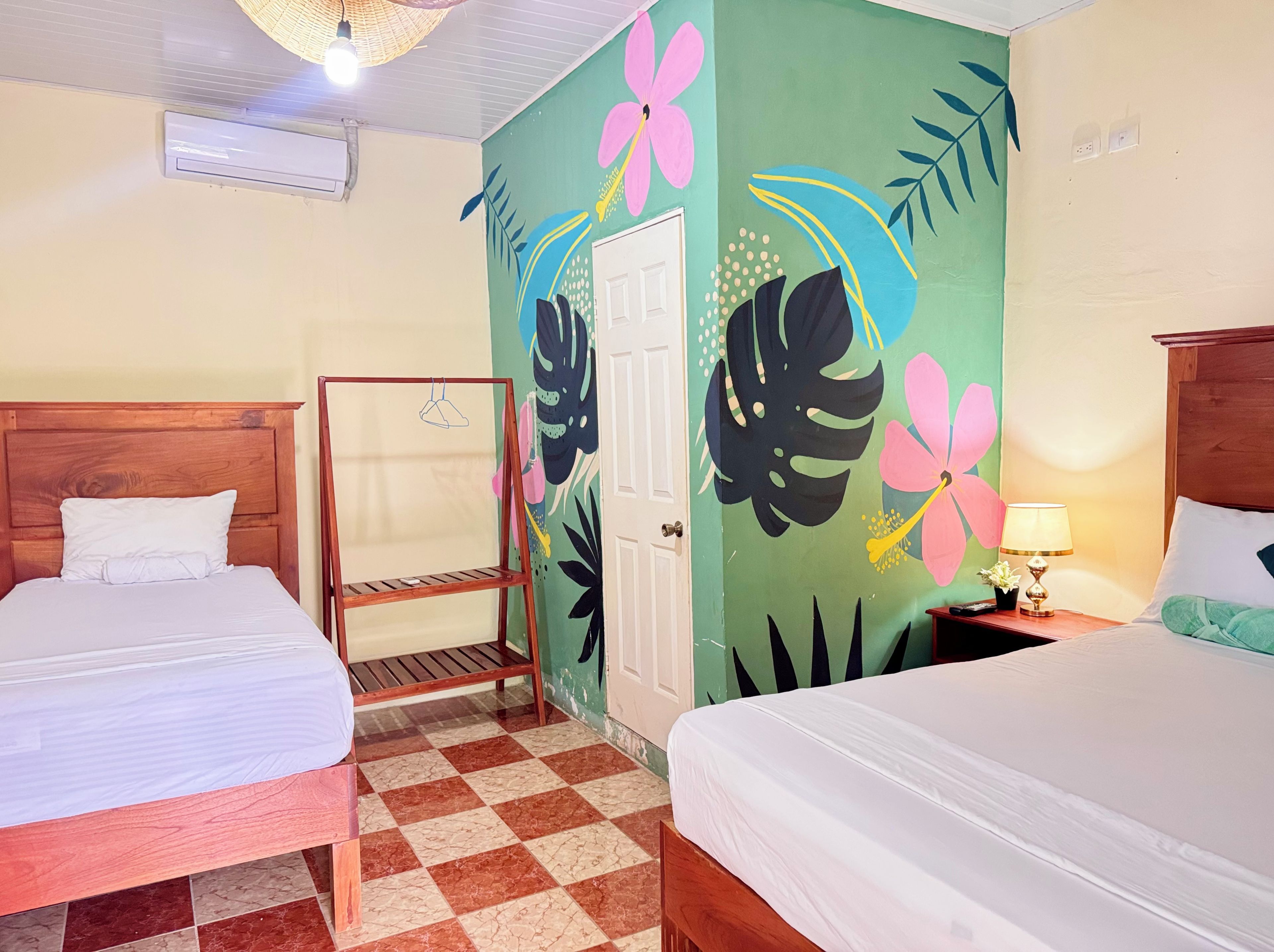 Een hotelkamer met twee bedden, een geruit vloerkleed, een deur en een muur met bloem- en bladmotieven.