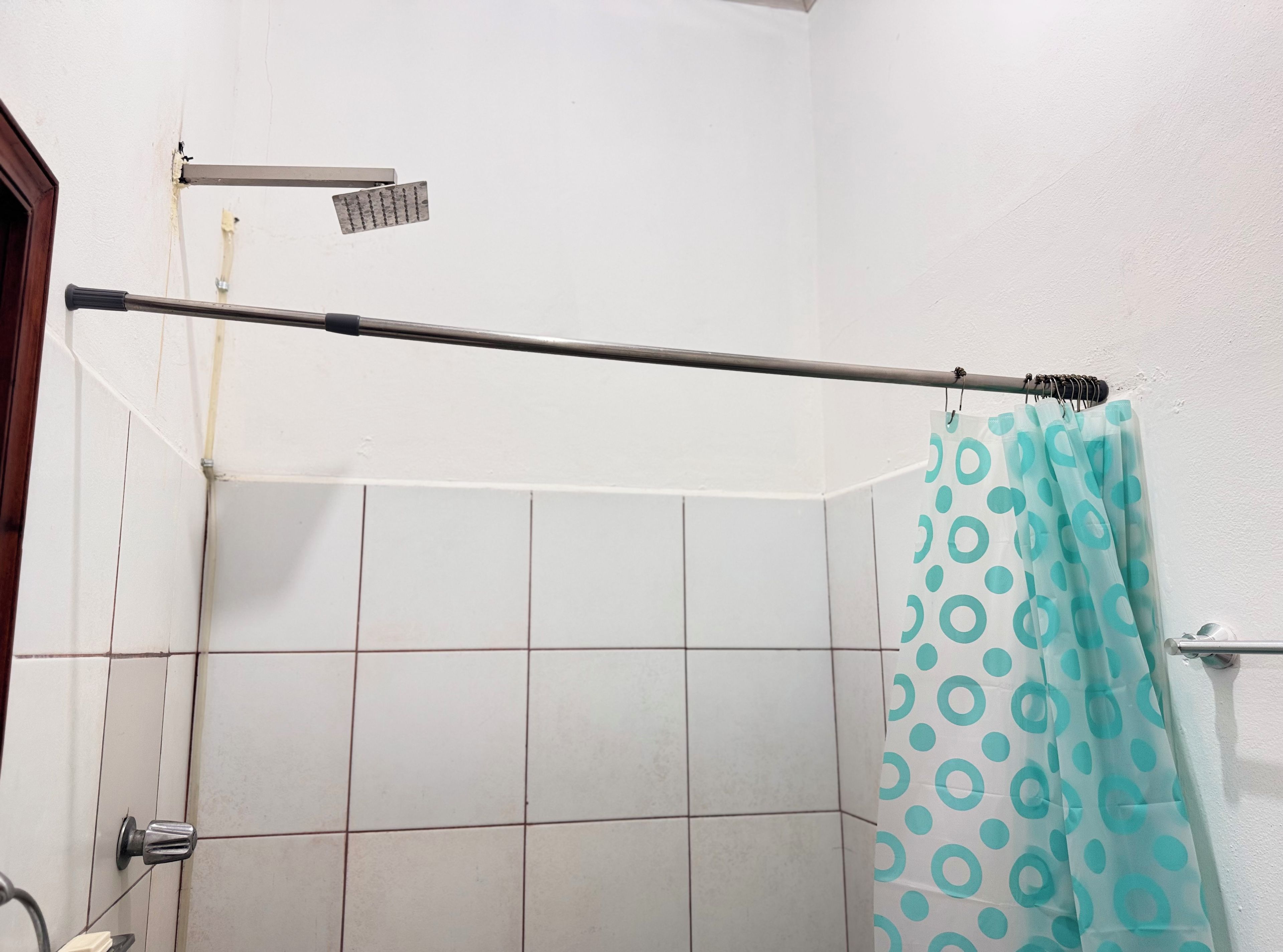 A bathroom with a shower curtain, a showerhead, and a towel rack.