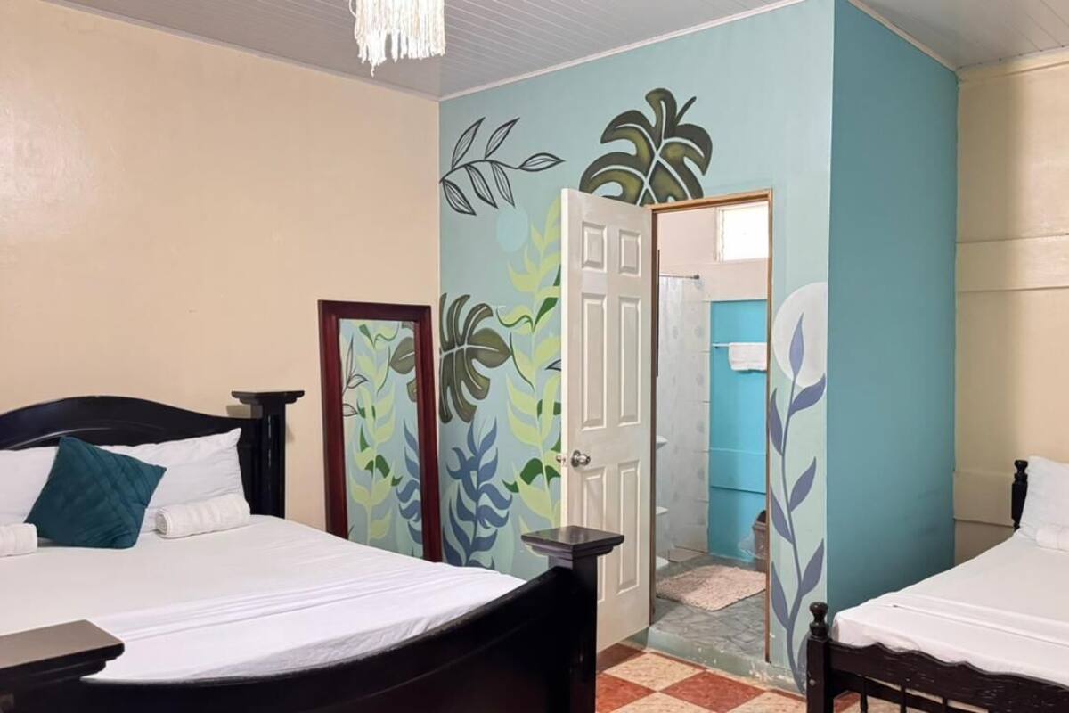 Een hotelkamer met twee bedden, een deur naar een badkamer en een muur met bladmotieven.