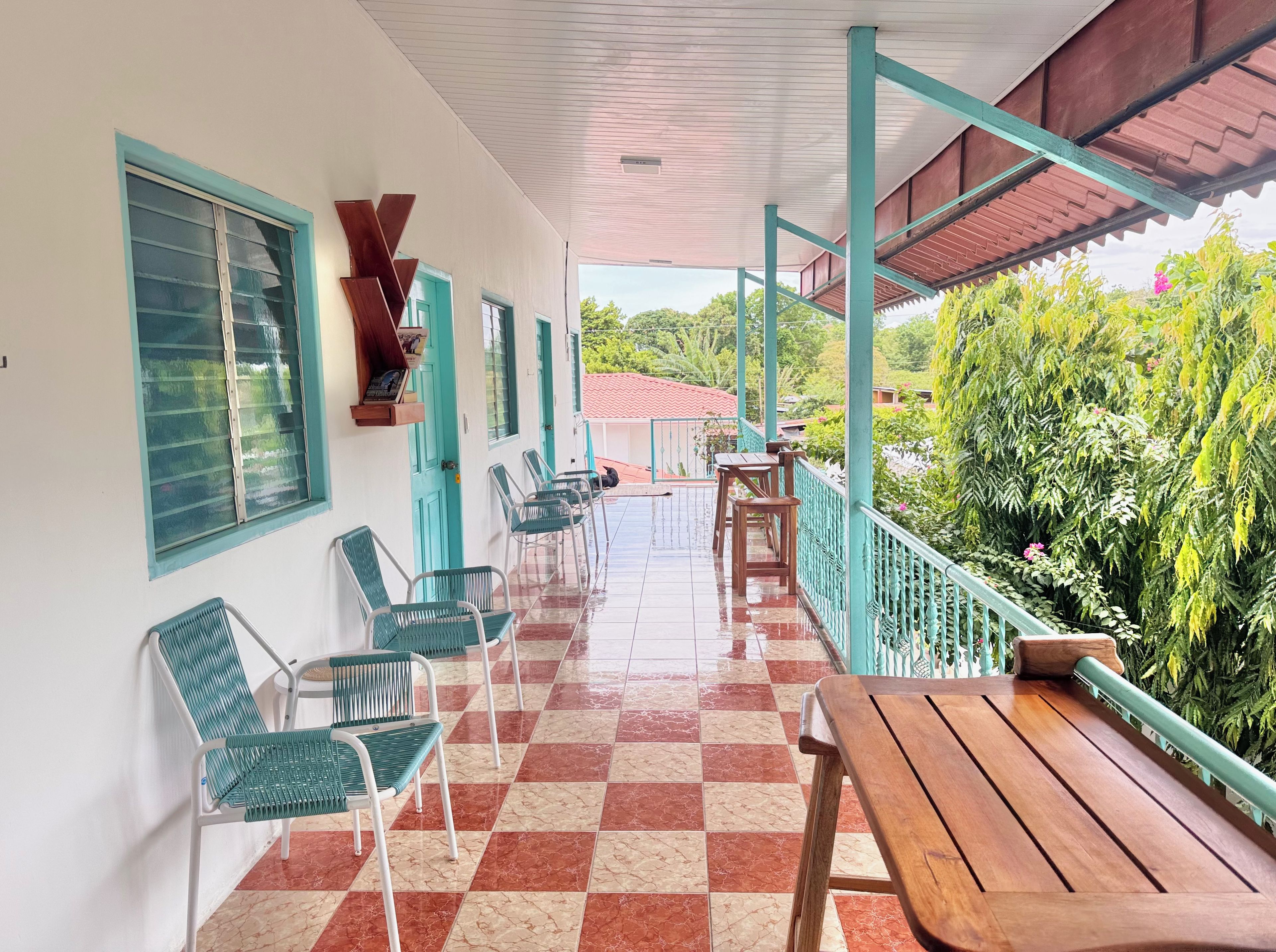 A covered outdoor seating area with chairs and tables, a tiled floor, and a view of greenery.