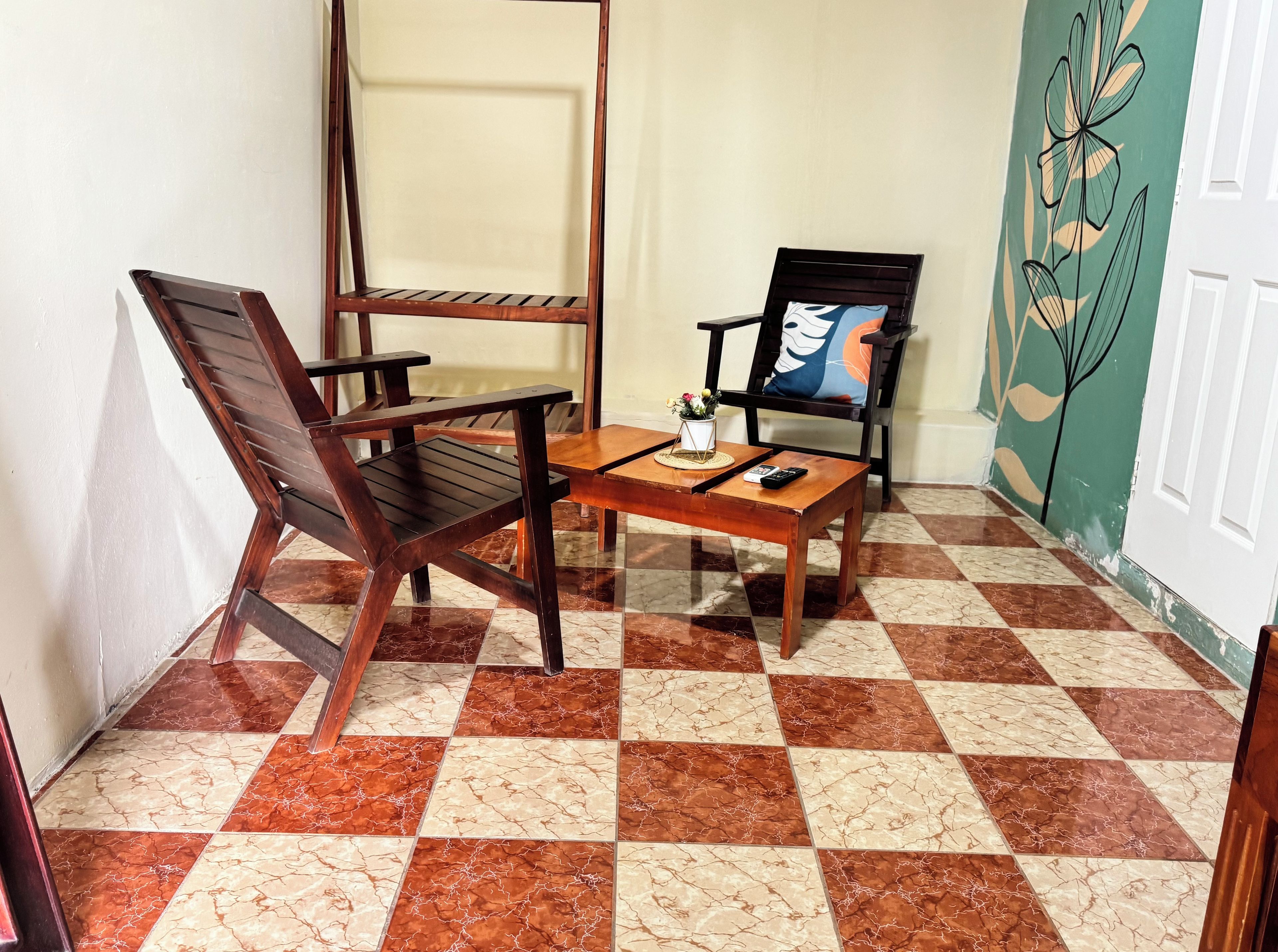 A corner room with a checkered floor, a wooden table, two chairs, and a wall with a floral design.