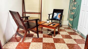 A corner room with a checkered floor, a wooden table, two chairs, and a wall with a floral design.