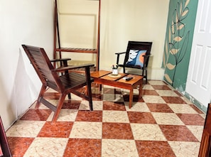 Une pièce d’angle avec un sol à carreaux, une table en bois, deux chaises et un mur orné d’un motif floral.
