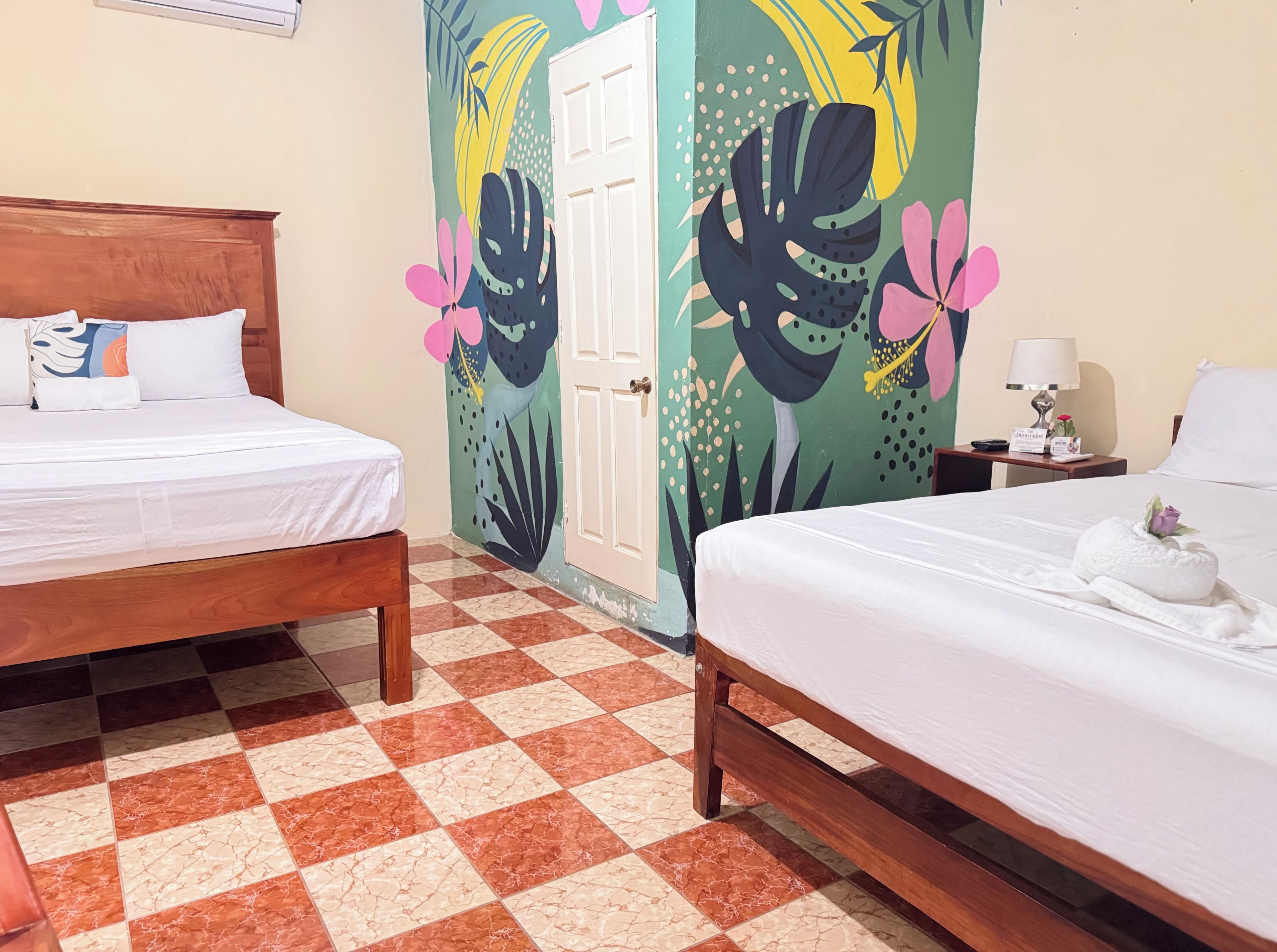 Une chambre d’hôtel avec deux lits, un sol à carreaux et une porte ornée d’une fresque colorée.