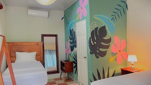 A room with two beds, a wooden headboard, a small table, a lamp, and a wall with floral and leaf patterns. - Hostal Eden Ometepe (Moyagalpa)
