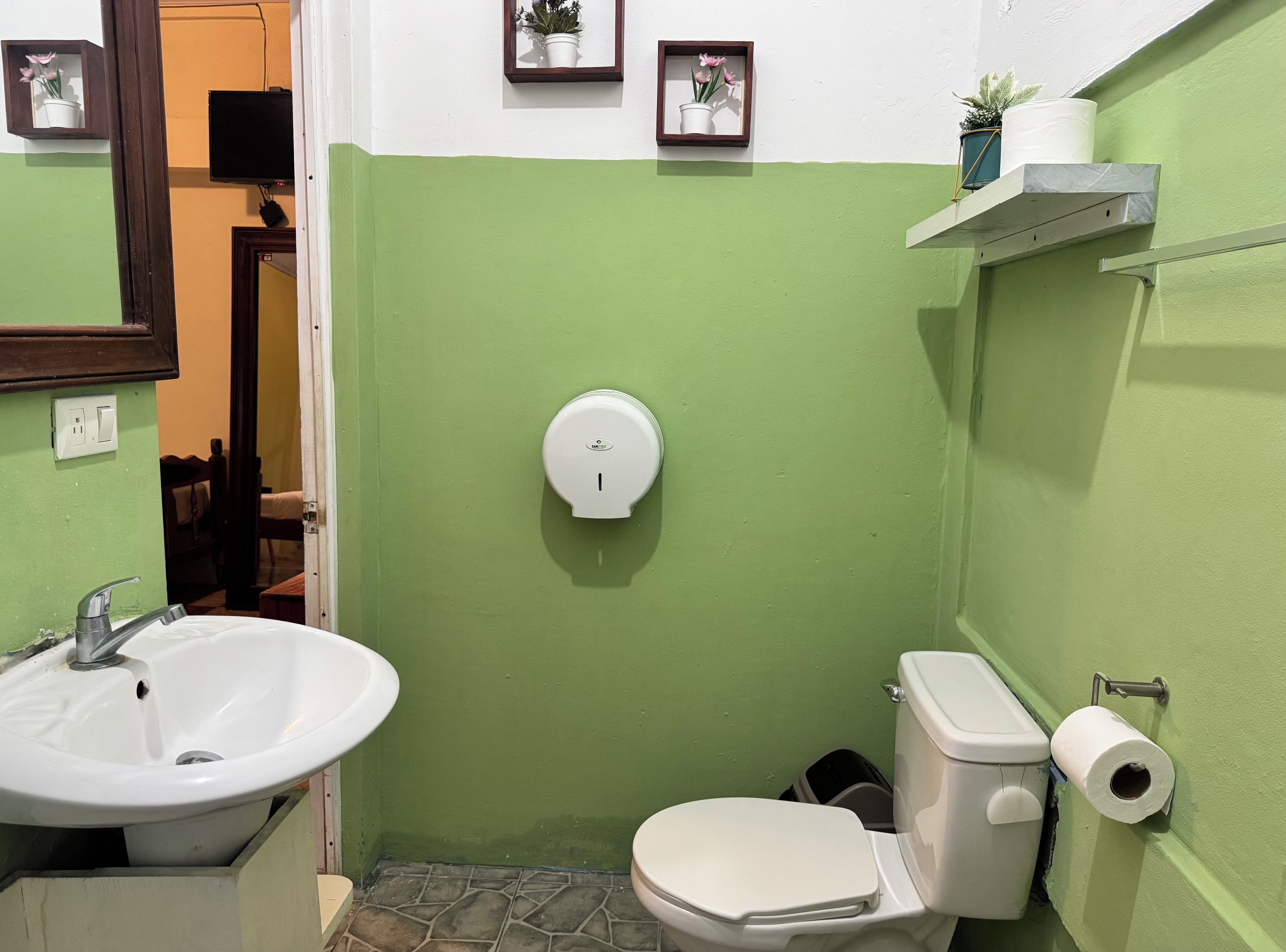 A bathroom with a green wall, a white sink, a toilet, and a hand dryer.