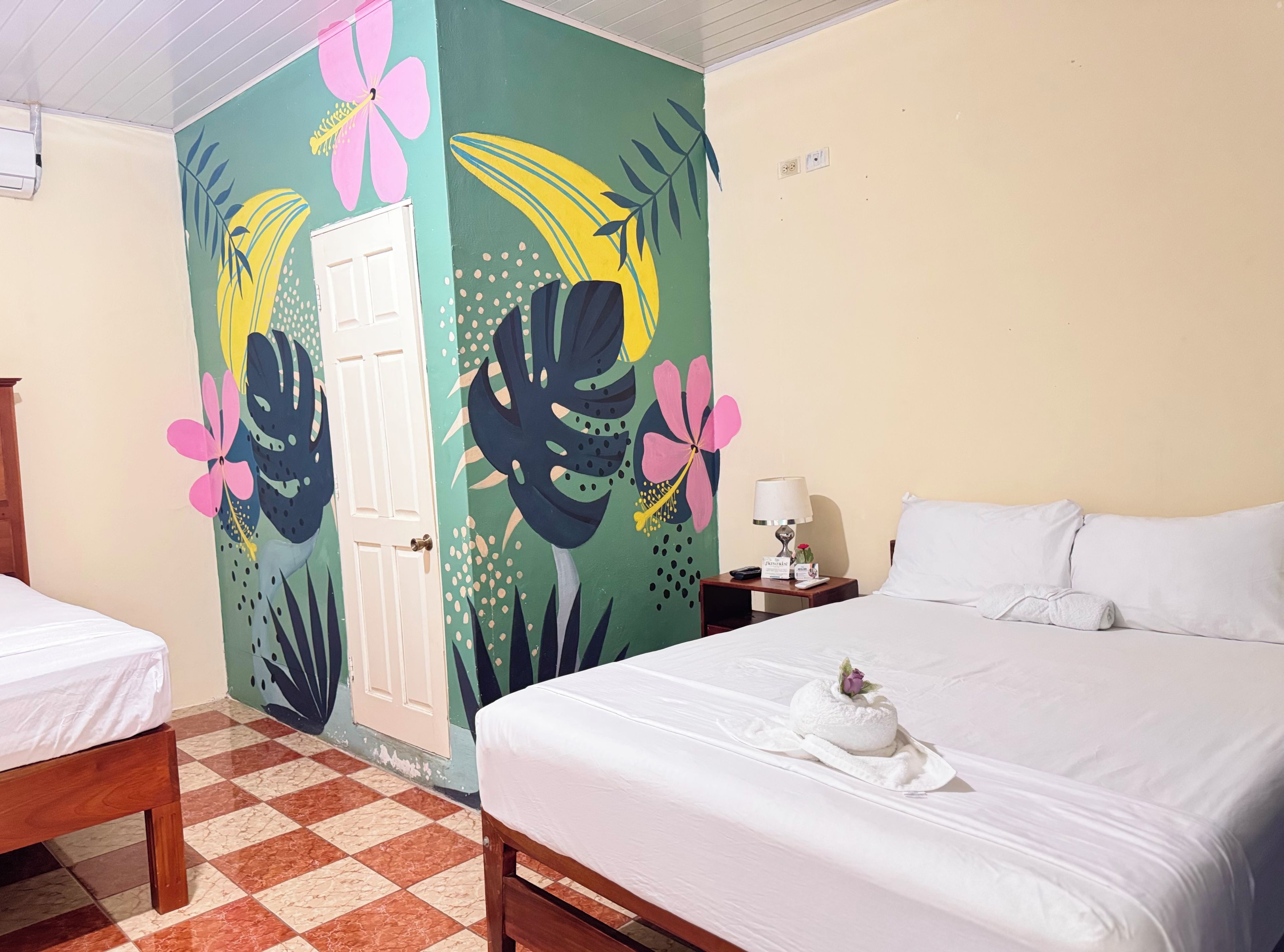 A hotel room with a bed, a nightstand, a lamp, and a door with a colorful mural.