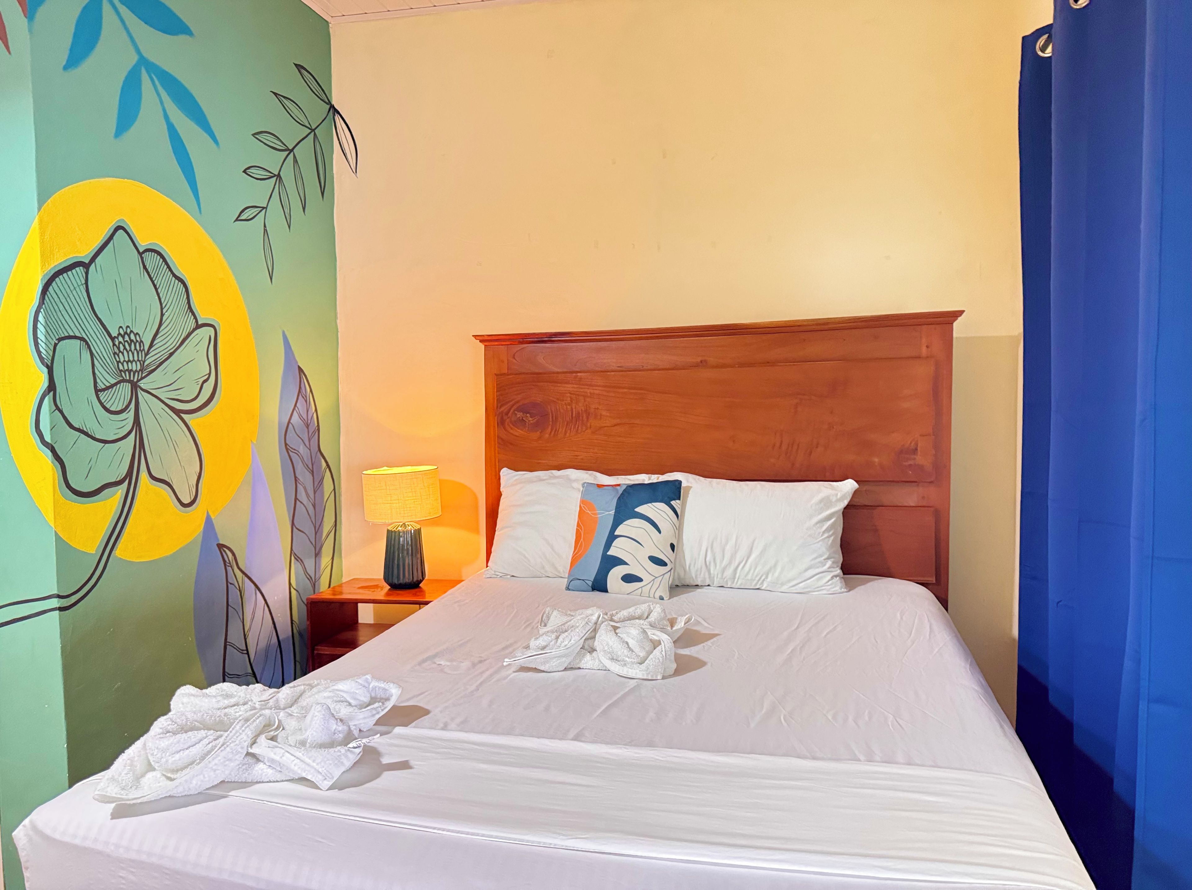 Une chambre d’hôtel avec un lit, des oreillers, une table de chevet avec une lampe et un mur orné d’une fresque florale.