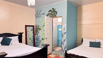 Habitación de hotel con dos camas, una puerta que da al baño y una pared con diseño de hojas.