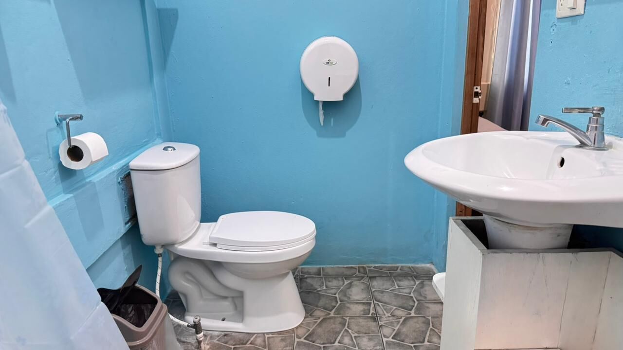 A bathroom with a toilet, a sink, a paper towel dispenser, and a trash bin.