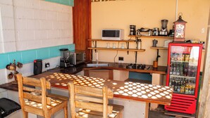 A kitchen with a wooden table, chairs, a microwave, a blender, a coffee maker, and a Coca-Cola refrigerator. - Hostal Eden Ometepe (Moyagalpa)