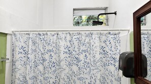Een badkamer met een douchegordijn met een bladmotief, een raam met uitzicht op groen en een wandgedroogde hand.'