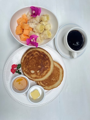 A breakfast plate with pancakes, fruit, and syrup, and a cup of coffee.