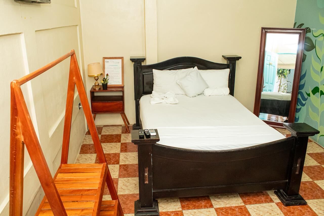 A room with a bed, a wooden chair, a nightstand with a lamp, and a mirror.
