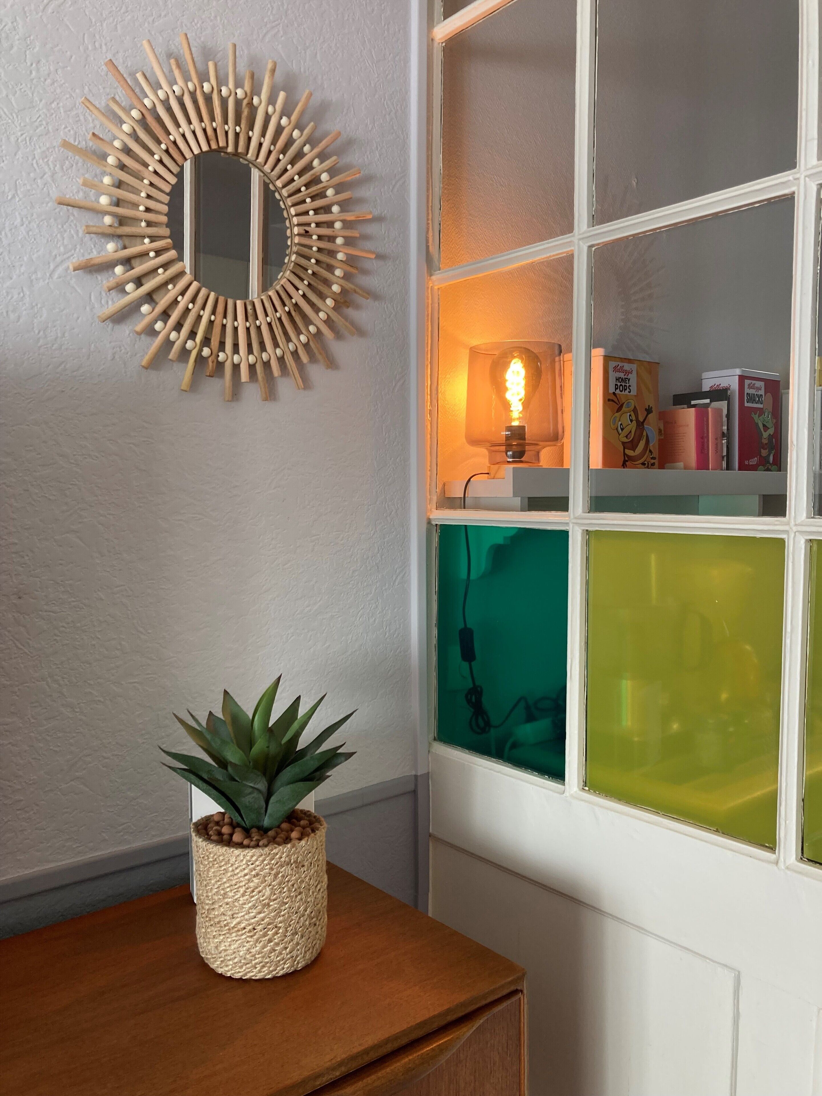A room with a wooden wall decor, a potted plant, and a window with colorful panes.
