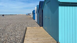 Een rij blauwe strandhutten met een houten looppad ernaartoe, gelegen op een kiezelstrand.