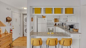 A modern kitchen with white cabinets, a granite countertop, and three yellow chairs.