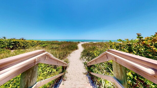 A wooden boardwalk leading to a beach with clear skies.