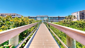 A wooden boardwalk leading to a building with multiple floors and large windows.
