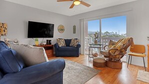 A modern living room with a blue sofa, a television, a ceiling fan, and a balcony with a view.