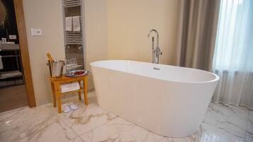 A modern bathroom with a freestanding bathtub, a wooden vanity with toiletries, and a towel rack.