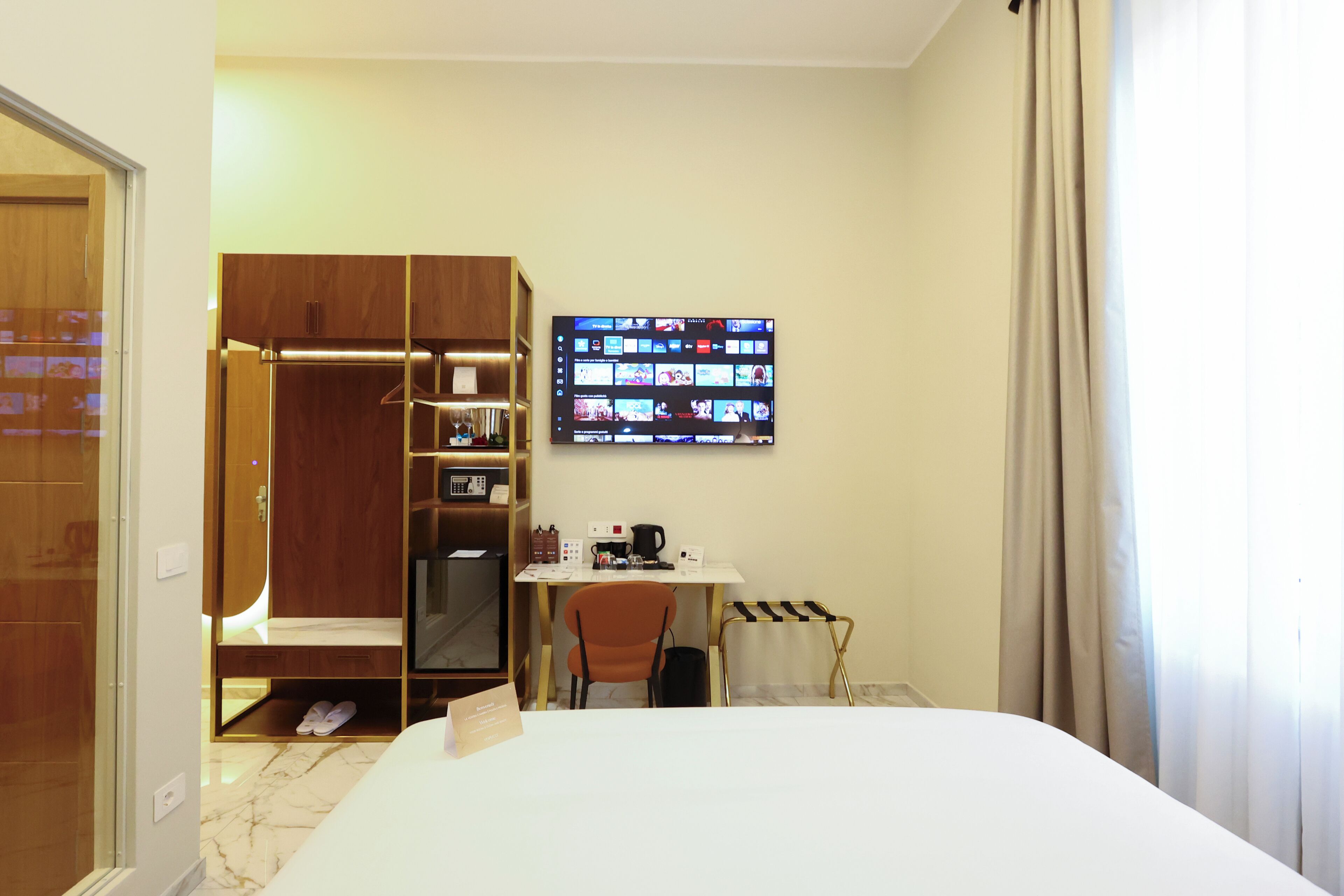 A hotel room with a bed, a desk with a computer, a TV mounted on the wall, and a closet.
