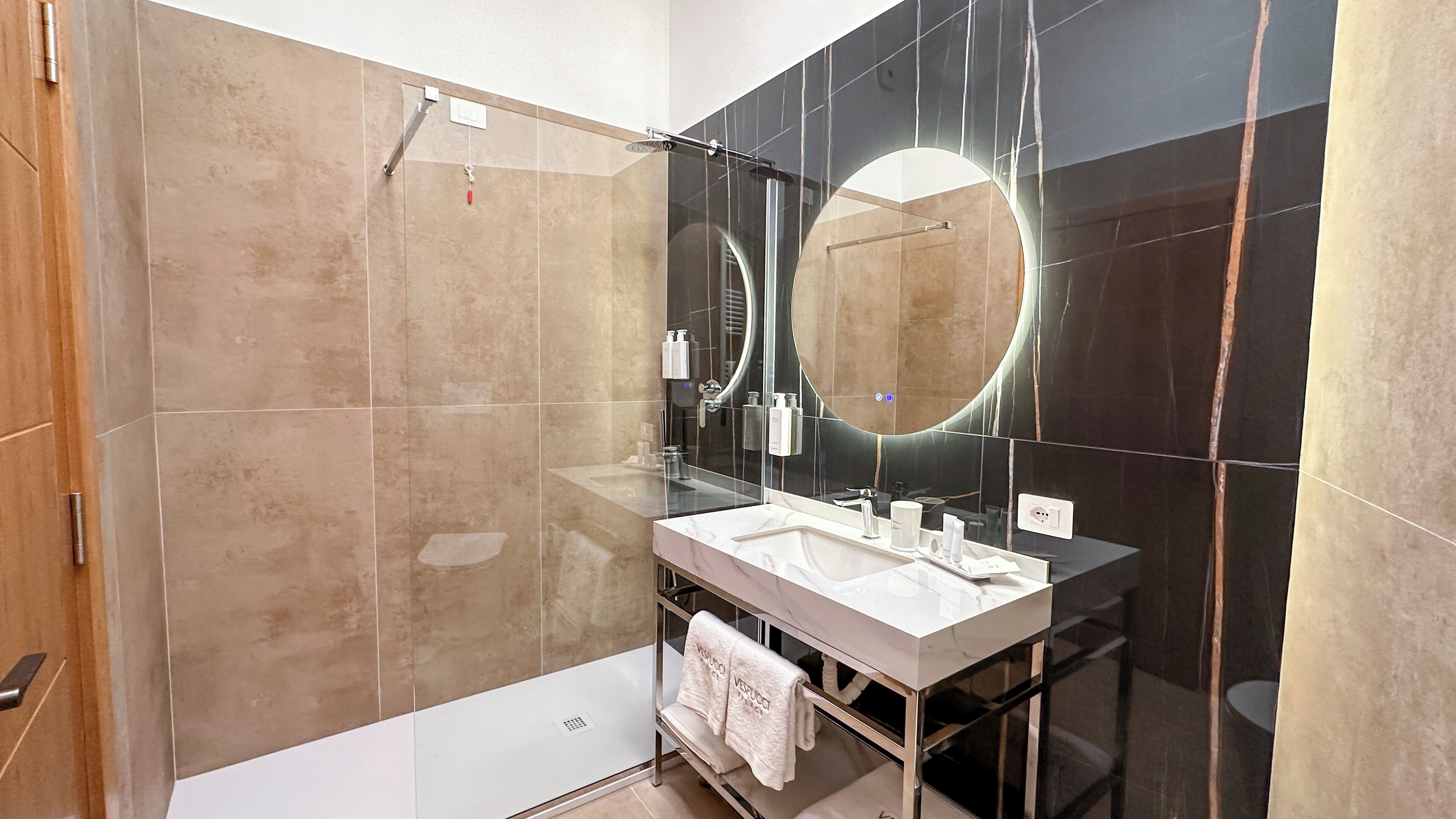 A modern bathroom with a glass shower enclosure, a large mirror, and a vanity with a white countertop.