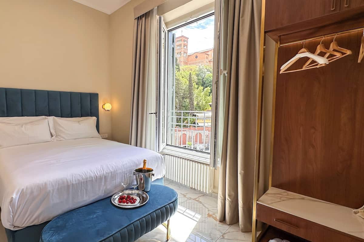 A hotel room with a bed, bedside table, and a view of a building through the window.