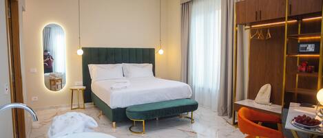 A hotel room with a bed, a bench, a chair, a table with fruit, a mirror, and a wardrobe.