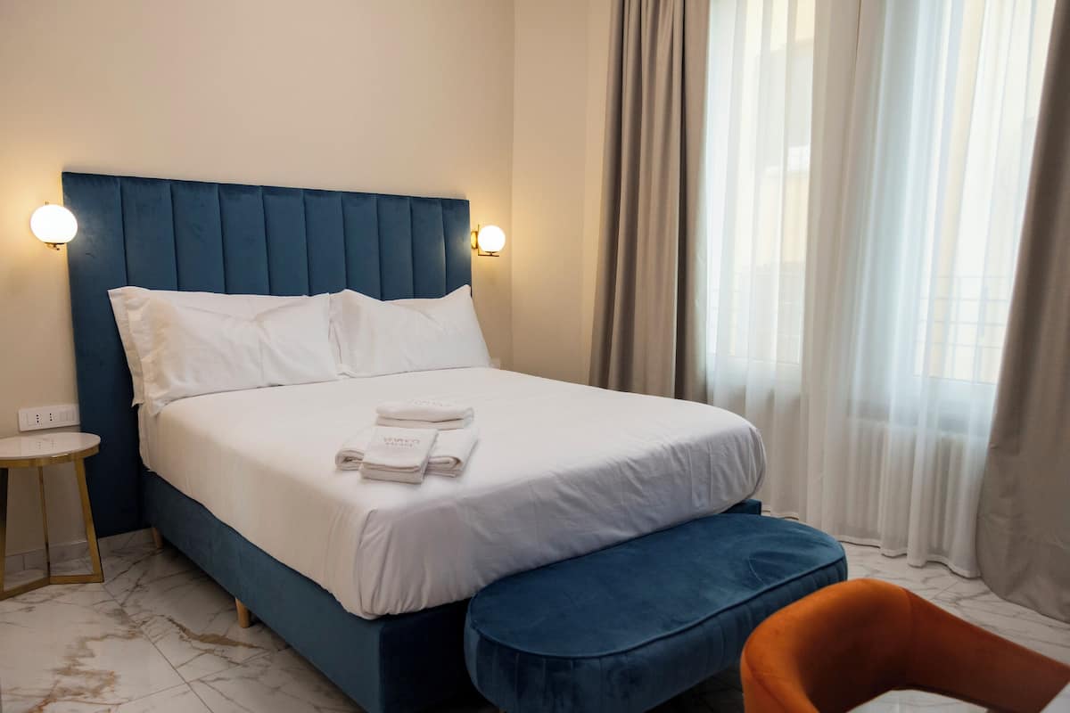 A hotel room with a large bed, a bedside table, a chair, and a window with curtains.