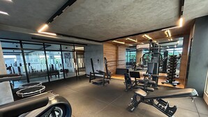 A gym with various exercise equipment, large windows, and a modern interior design. - Co-House (João Pessoa)