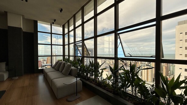 A modern living room with a large window, a sofa, and a plant shelf. - Co-House (João Pessoa)