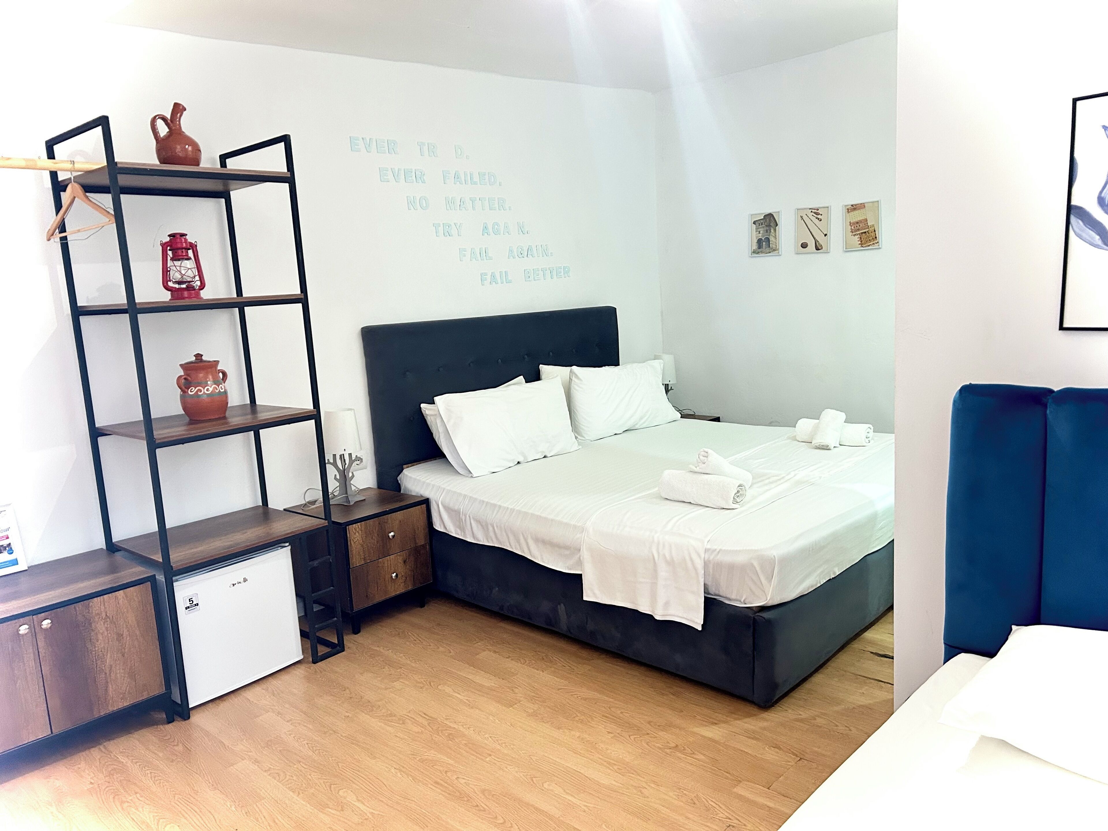 Un dormitorio ordenado con una cama, una estantería decorada, una mesita de noche y una pared con texto motivacional.