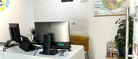 Un espacio de oficina moderno con una computadora de escritorio Dell, un cojín amarillo, un mapa en la pared y una planta en maceta.