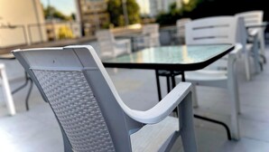 A modern outdoor seating area with a glass table and white chairs. - Tirana Budget Retreat Hotel (Tirana)