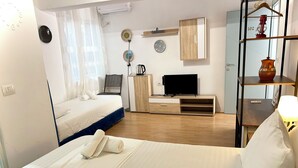 A hotel room with a bed, a TV, a desk, and a shelf with decorative items. - Tirana Budget Retreat Hotel (Tirana)