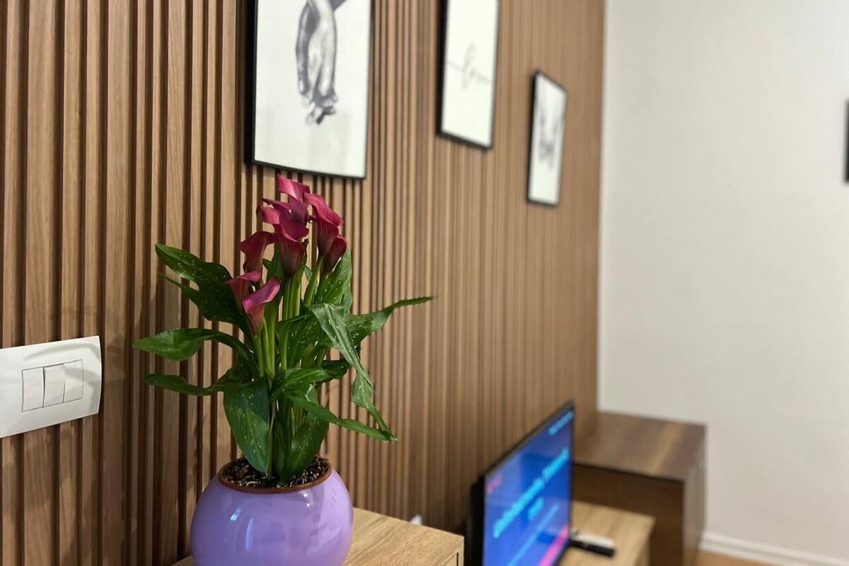 Una habitación con una pared de madera, un jarrón morado con flores y un televisor sobre un mueble de madera.