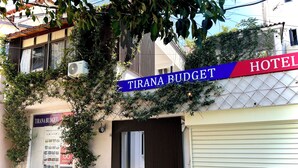 A hotel named "TIRANA BUDGET" with a signboard, a closed shutter door, and some greenery around the entrance. - Tirana Budget Retreat Hotel (Tirana)
