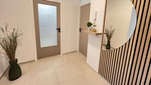 A hallway with a door, a mirror, and a shelf with plants. - Rosoglio Poreč 300m from sea, new apartment 2024 (Poreč)