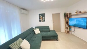 A modern living room with a sectional sofa, a flat-screen TV, and a decorative shelf. - Rosoglio Poreč 300m from sea, new apartment 2024 (Poreč)