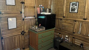 Ein Zimmer mit Holzvertäfelung, einem grünen Schrank mit Schubladen, einem schwarzen Kühlschrank, einer kleinen Mülltonne und einem Tisch mit einer Laterne.